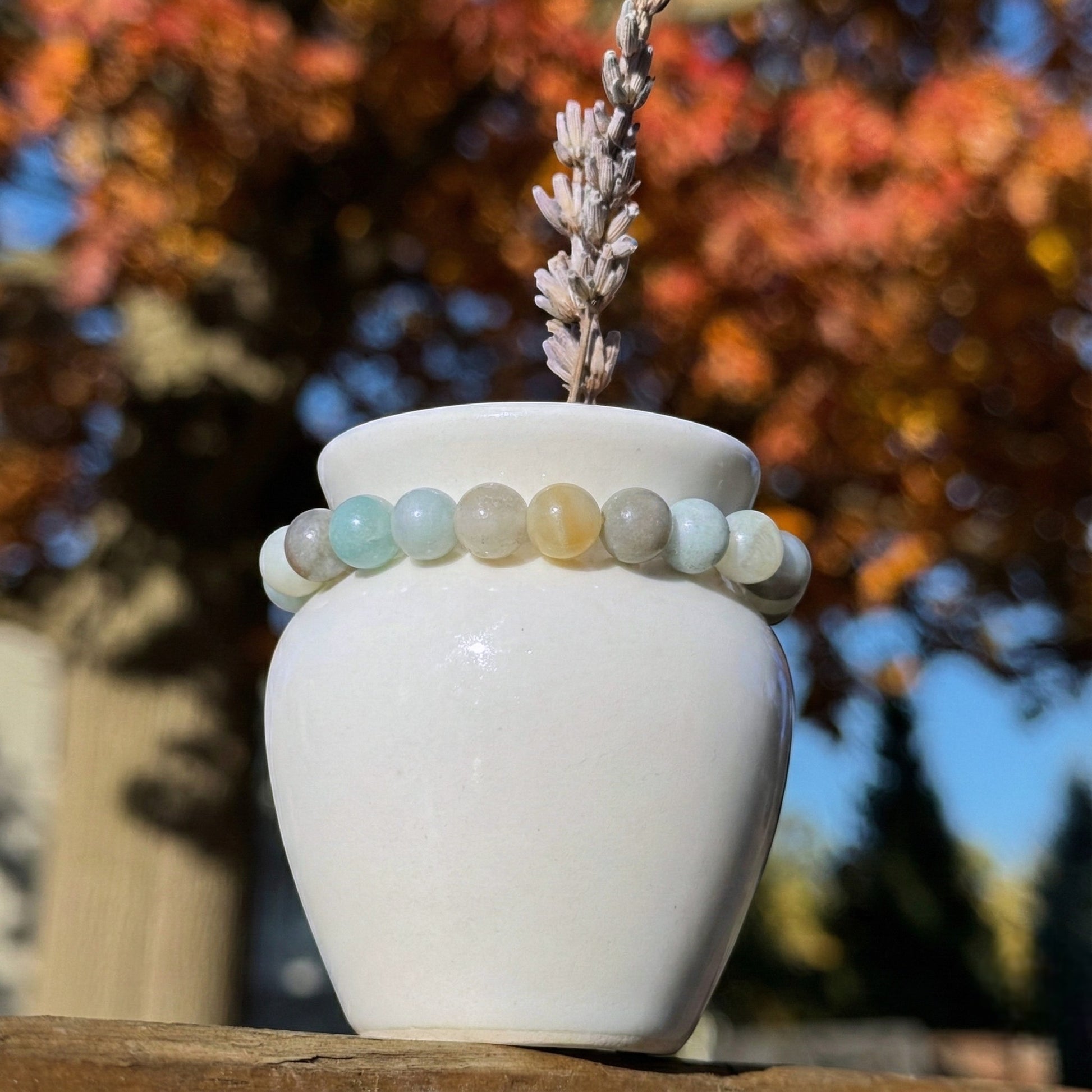 White vase with an amazonite bracelet on top against a blurred autumn tree background